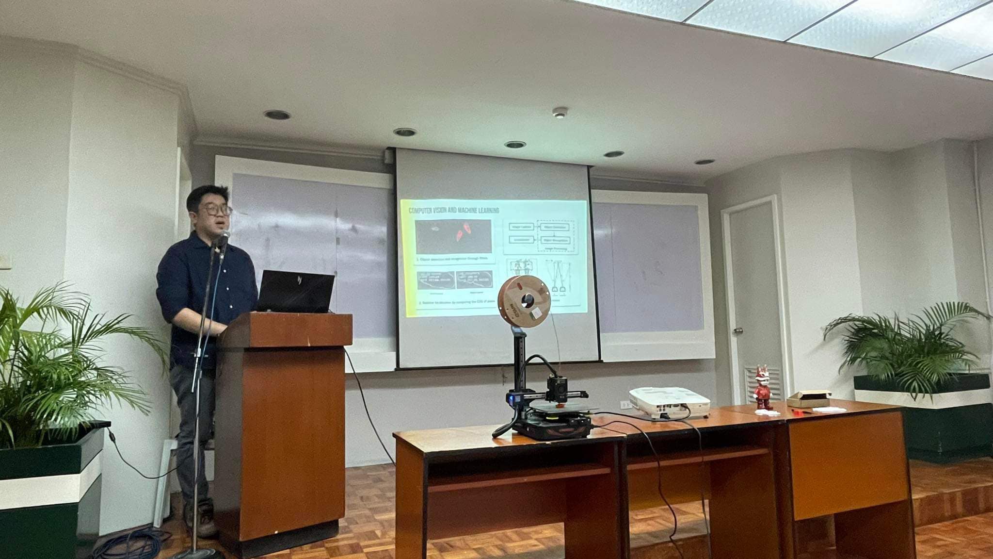 Charles Lu presenting with an active 3D printer running live on the stage table at UE Manila